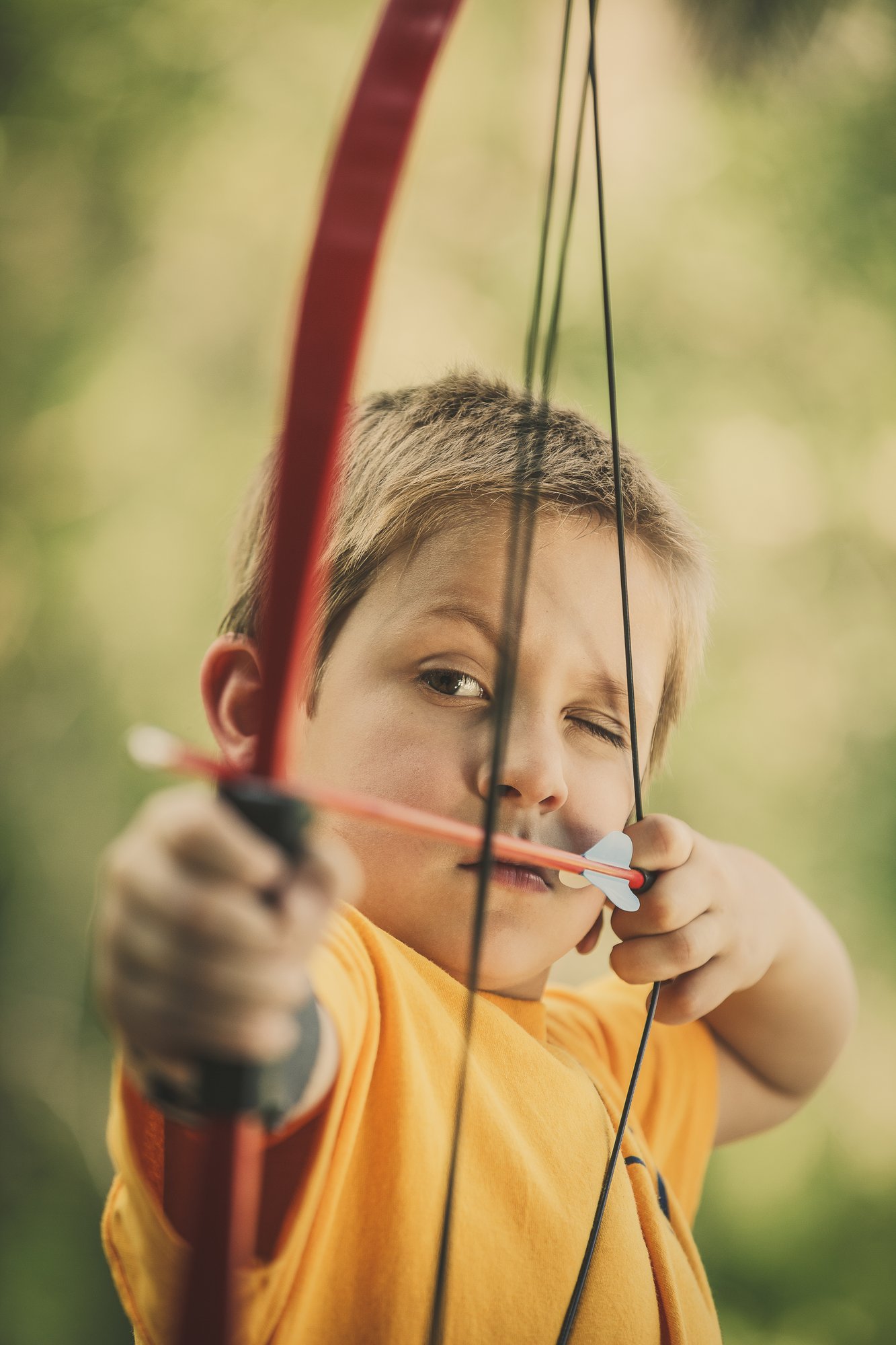 A young Cub Scout focused on aiming a bow at archery practice